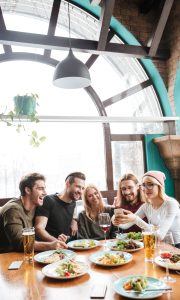 Photo of happy friends sitting in cafe and drinking alcohol while using mobile phone.