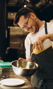 Chef at kitchen in a restaurant adding sauce to the salad